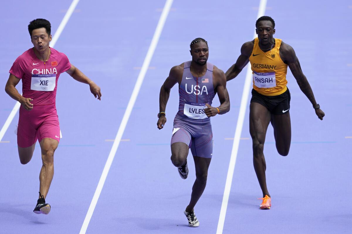 U.S. sprinter Noah Lyles runs alongside two competitors in a men's 100 meters heat at the Paris Olympics.