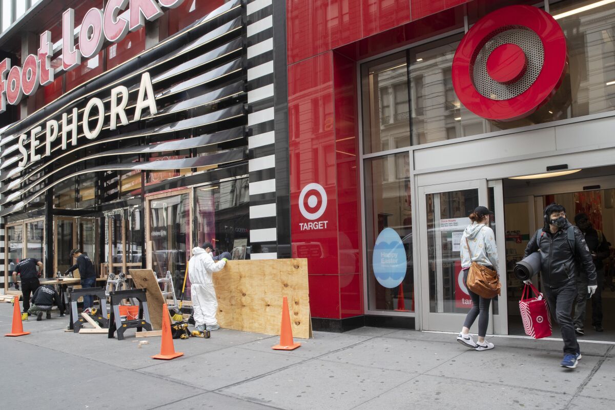 FILE - In this Friday, March 20, 2020 file photo, a shopper leaves the Target Store on 34th St. with supplies as carpenter board up the Sephora story in New York. Target Corp. said Friday it will give a $2 an hour wage increase to its 300,000-plus workers who have been scrambling to help customers. The pay bump will be effective at least through May 2. (AP Photo/Mary Altaffer, File)