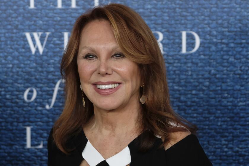 A woman with long hair in a black dress with white accents smiles upon arrival at an event