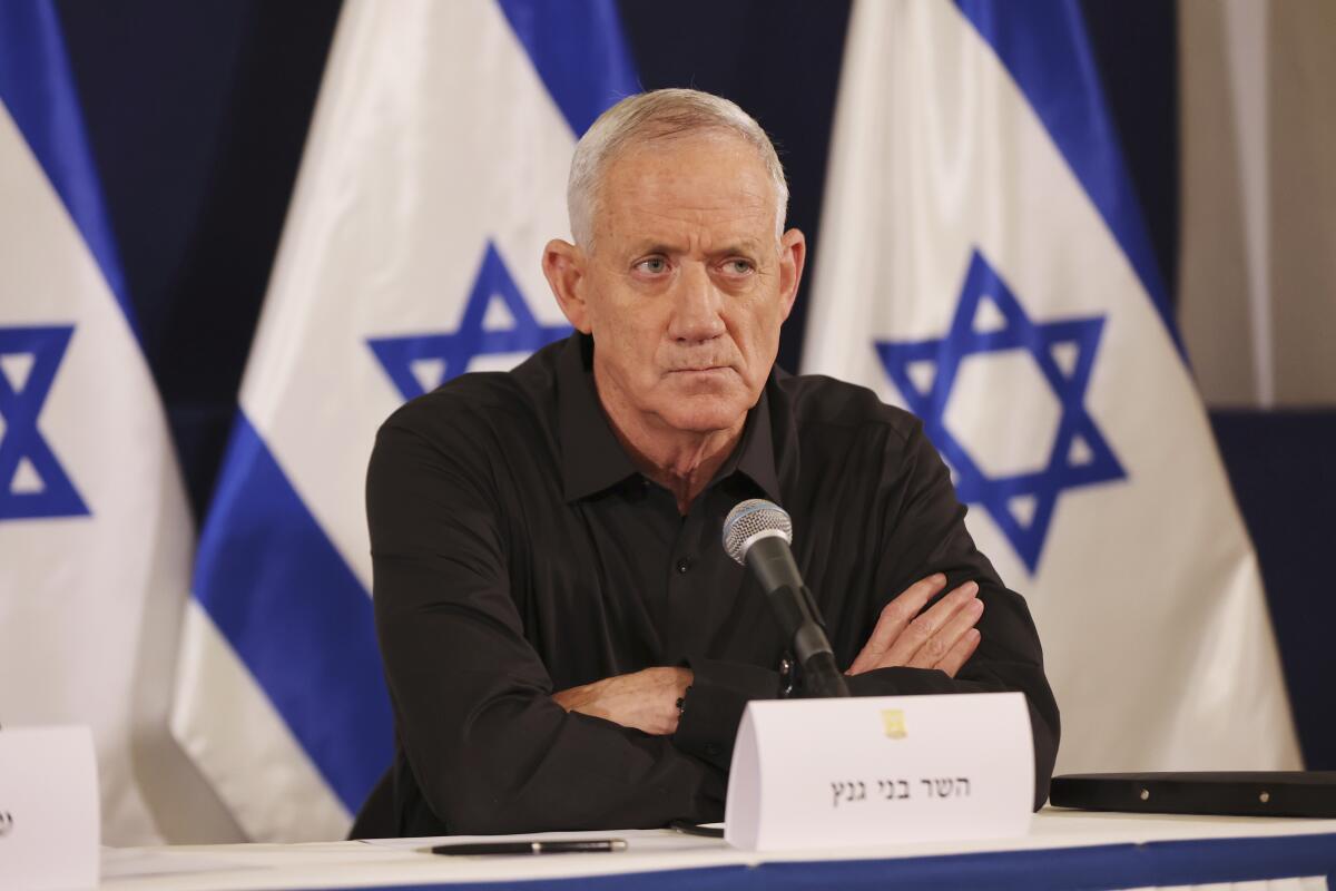 Israeli Cabinet member Benny Gantz sits with his arms folded with Israeli flags in the background.