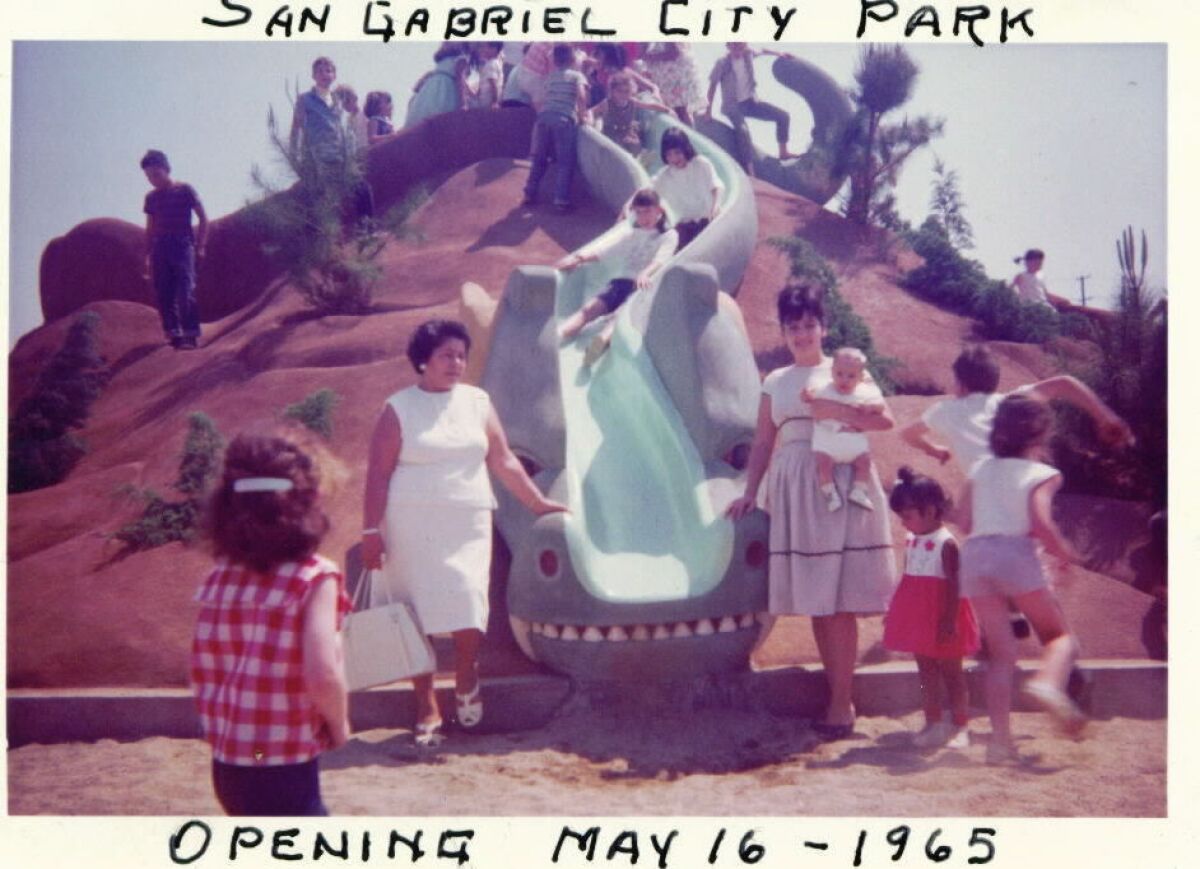 Women stand next to a curving slide as children slide down.