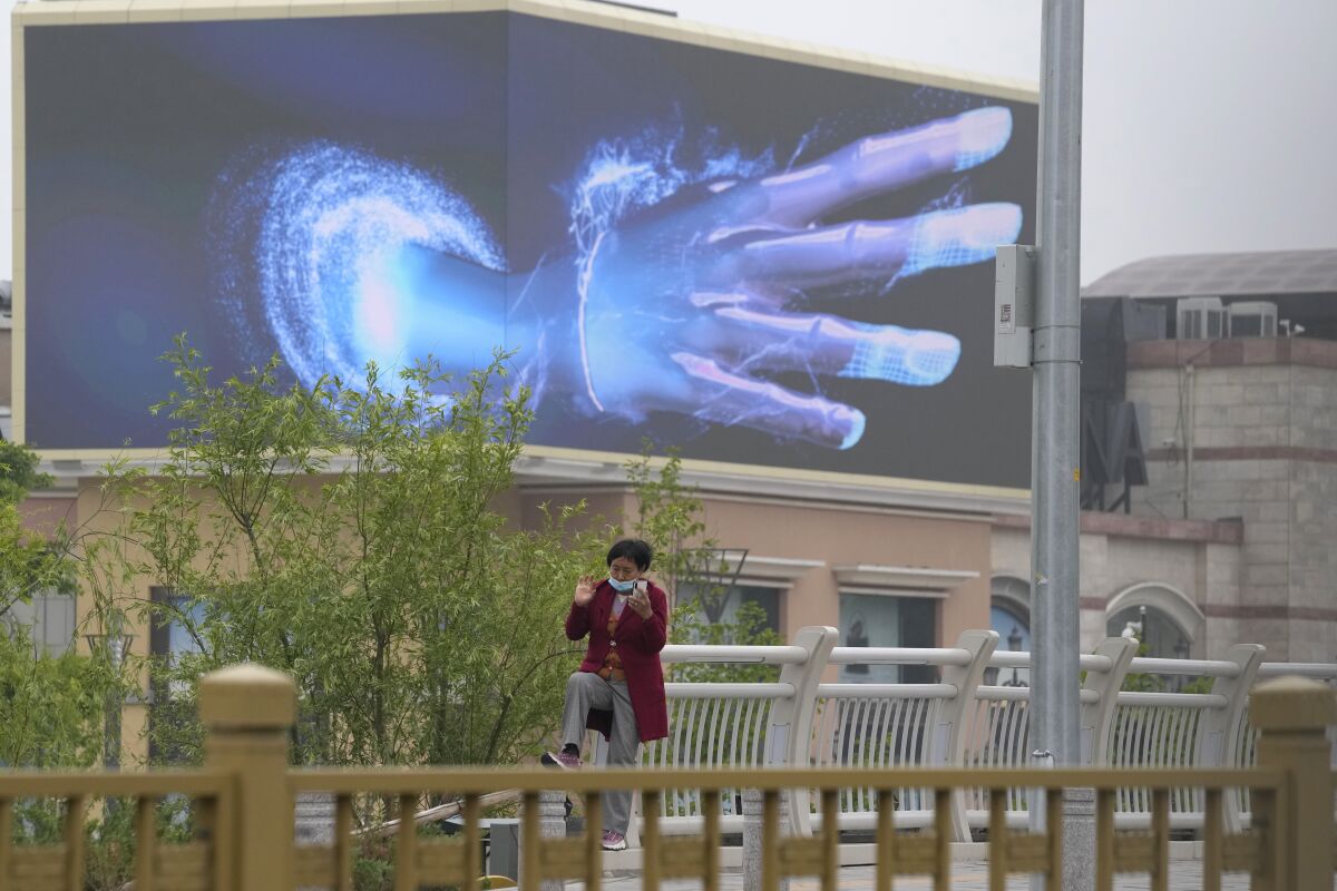 Una mujer habla por su celular cerca de una pantalla con una imagen de una mano en un centro comercial vacío con tiendas cerradas, el 10 de mayo de 2022, en Beijing. (AP Foto/Ng Han Guan)