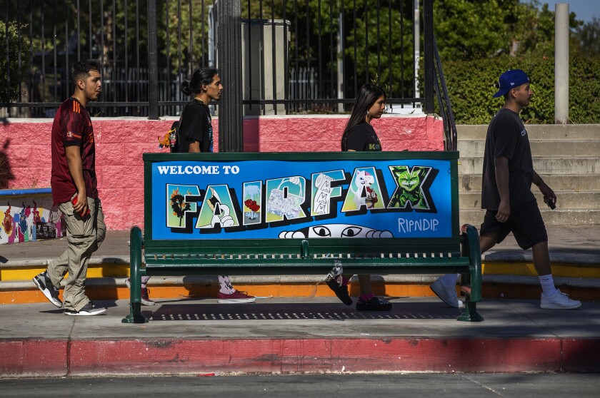 Four people walk behind a bench that reads Fairfax.