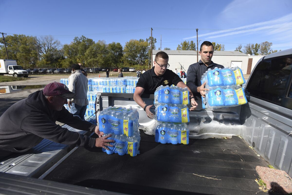 From left, Dave MacDonald, Michigan State Trooper Charles Scruggs and Trooper David Williams join volunteers as they distribute water Wednesday, Oct 27, 2021, at the Southwest Michigan Community Action Agency in Benton Harbor, Mich. City residents are advised to not drink water due to possible contamination from homes' lead pipes. (Don Campbell/The Herald-Palladium via AP)