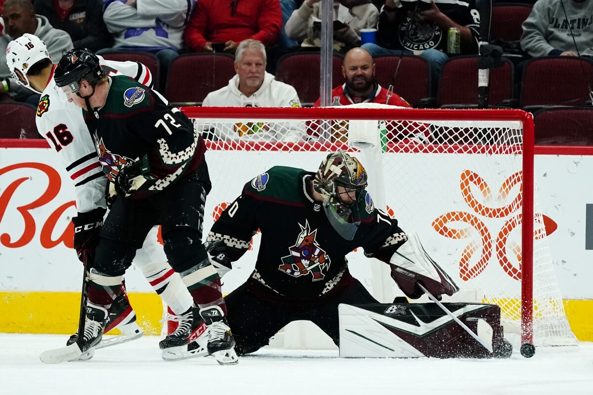 Arizona Coyotes goaltender Karel Vejmelka, right, makes a save as Coyotes center Travis Boyd (72) and Chicago Blackhawks left wing Jujhar Khaira battle for position during the first period of an NHL hockey game Thursday, Jan. 6, 2022, in Glendale, Ariz. (AP Photo/Ross D. Franklin)