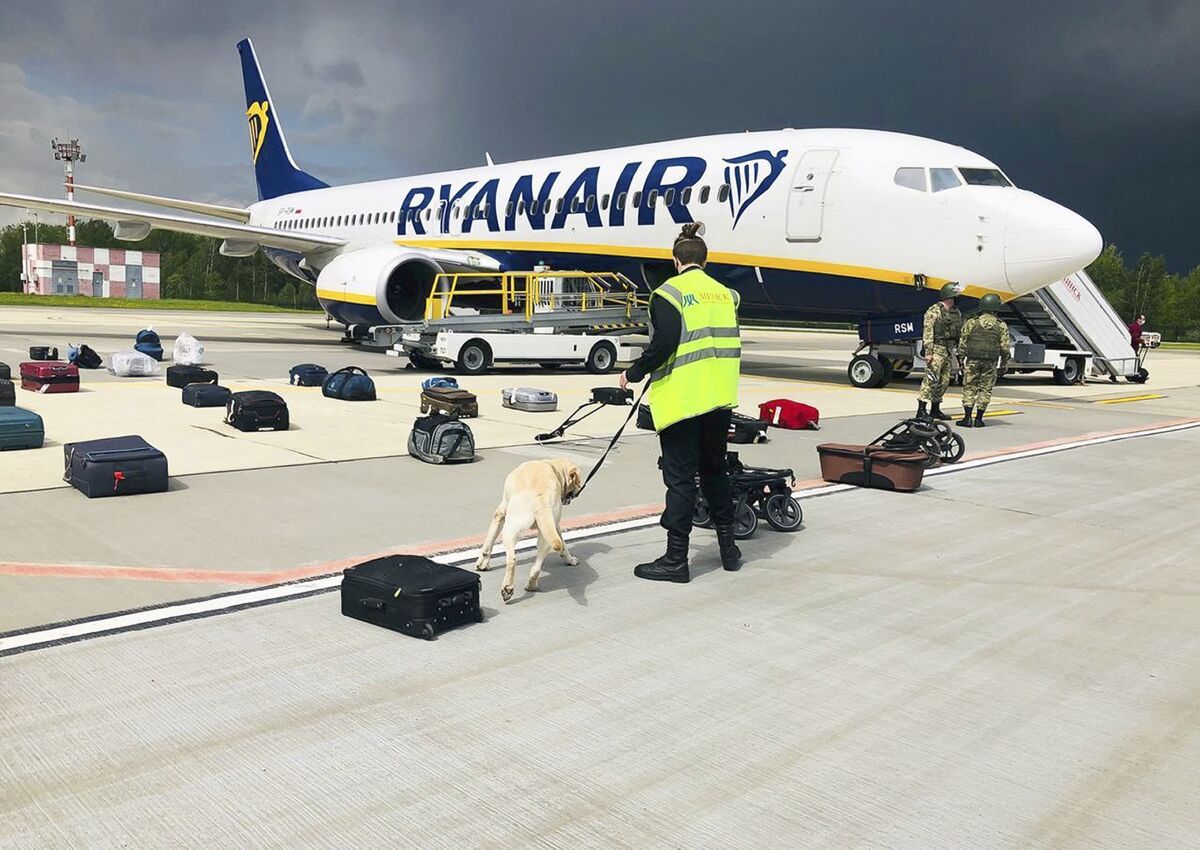 Ryanair plane on a tarmac with soliders nearby and a person with a dog on a leash