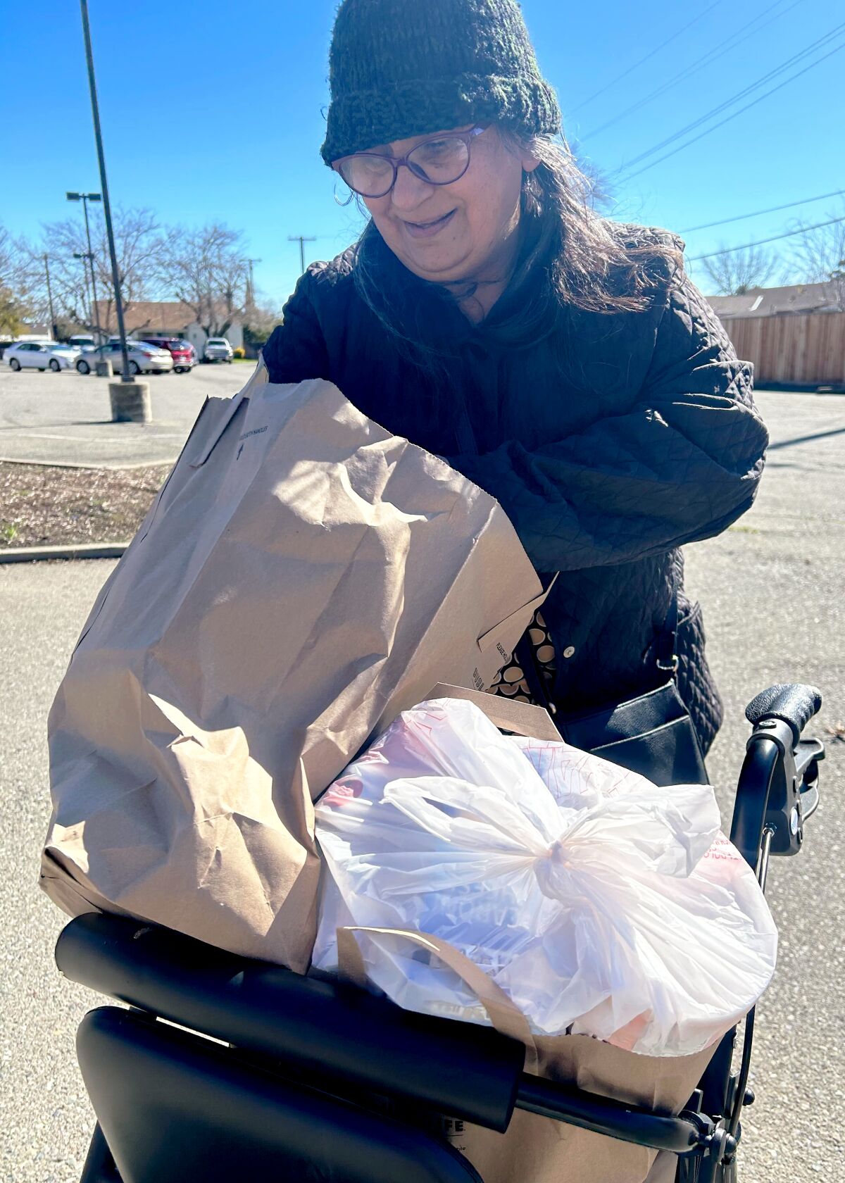 Standing outside, Delia Priscilla Ortega Darden looks through a paper bag with groceries 