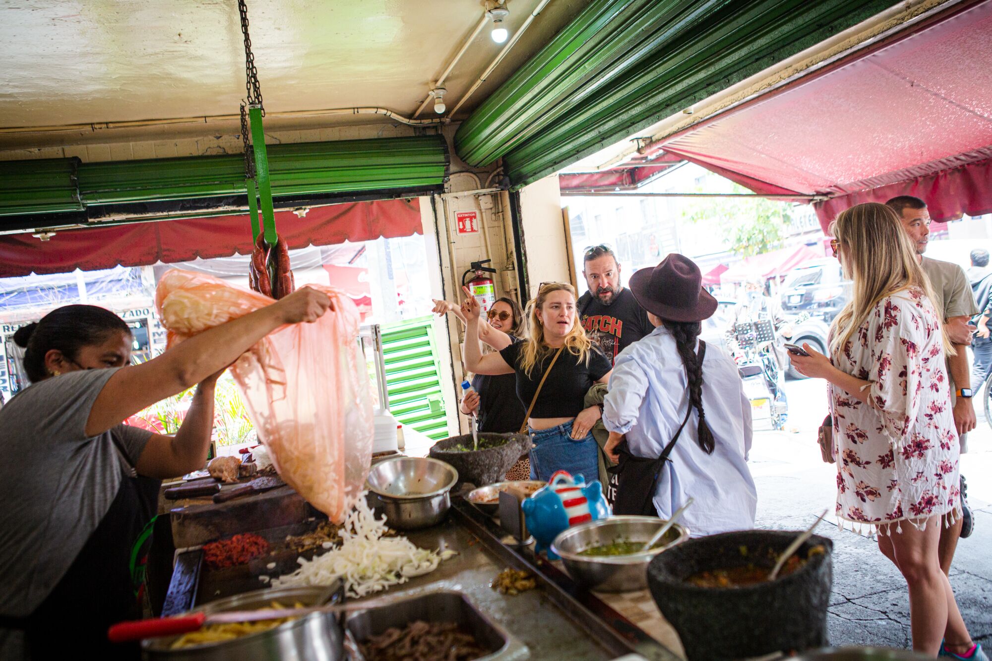 Customers gather at Ricos Tacos Toluca as a cook pours ingredients from a plastic bag, 