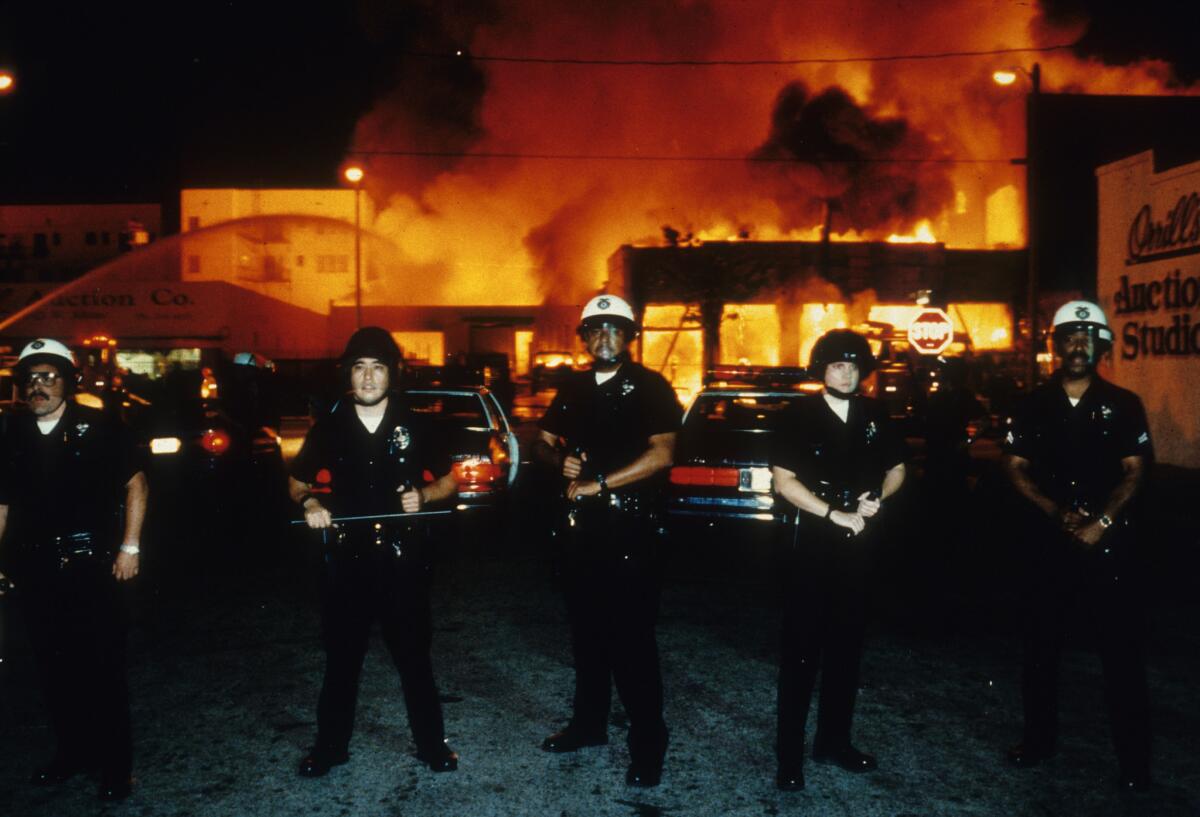 Officers stand guard as fire units battle a blaze near 19th Street and Adams Boulevard on April 30, 1992. (Los Angeles Times)