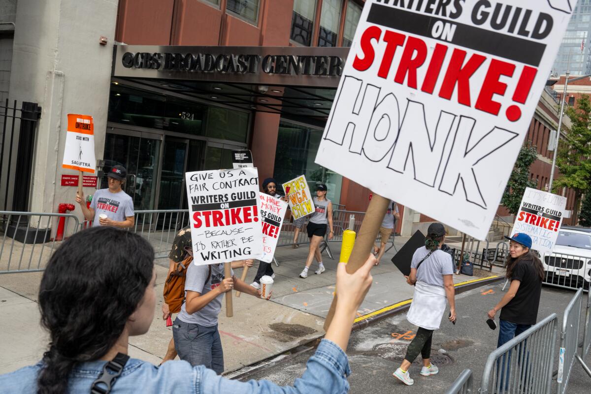 Picketers carry signs that say Writers Guild on Strike outside a theater
