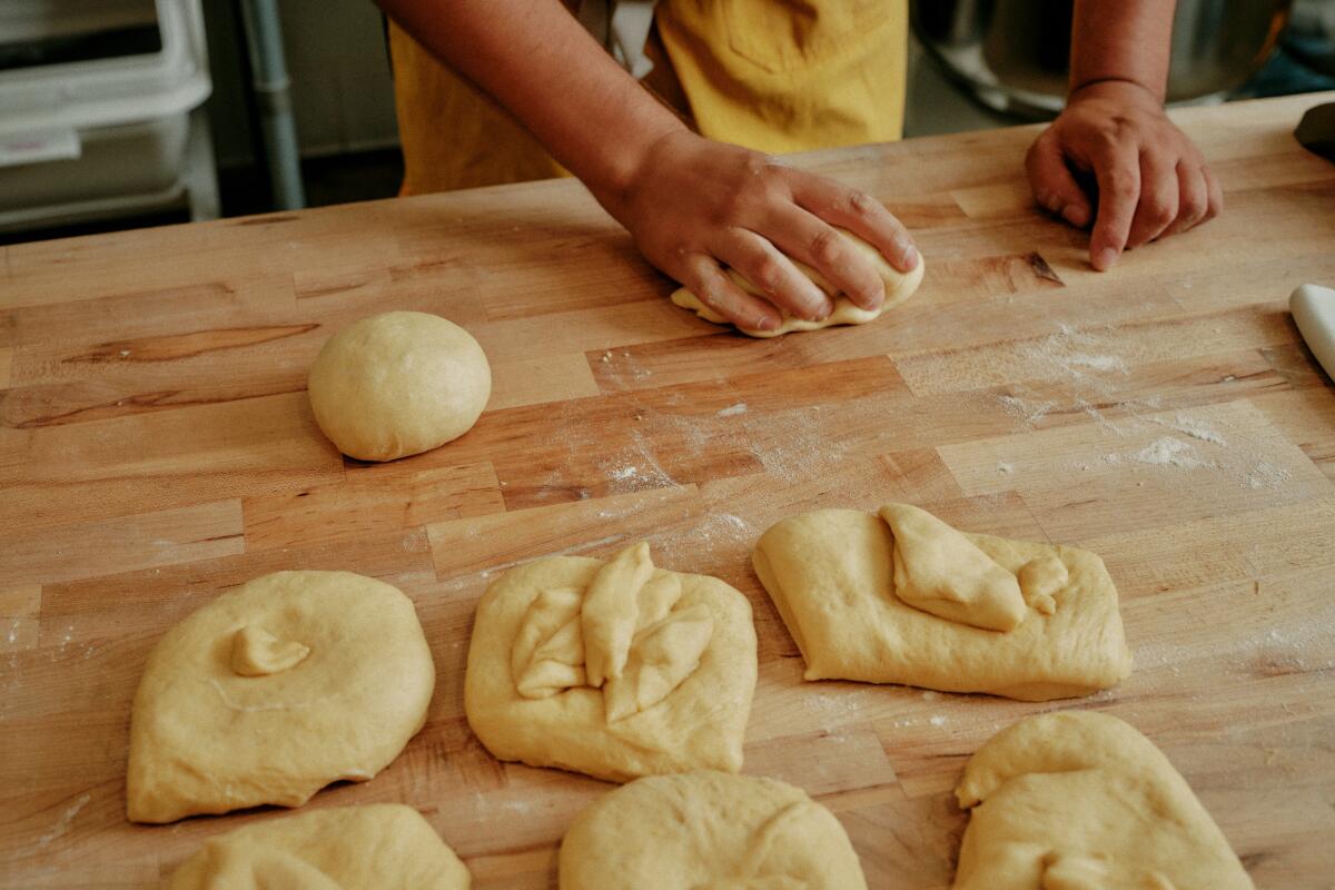 Hands working smaller pieces of pan de muerto dough