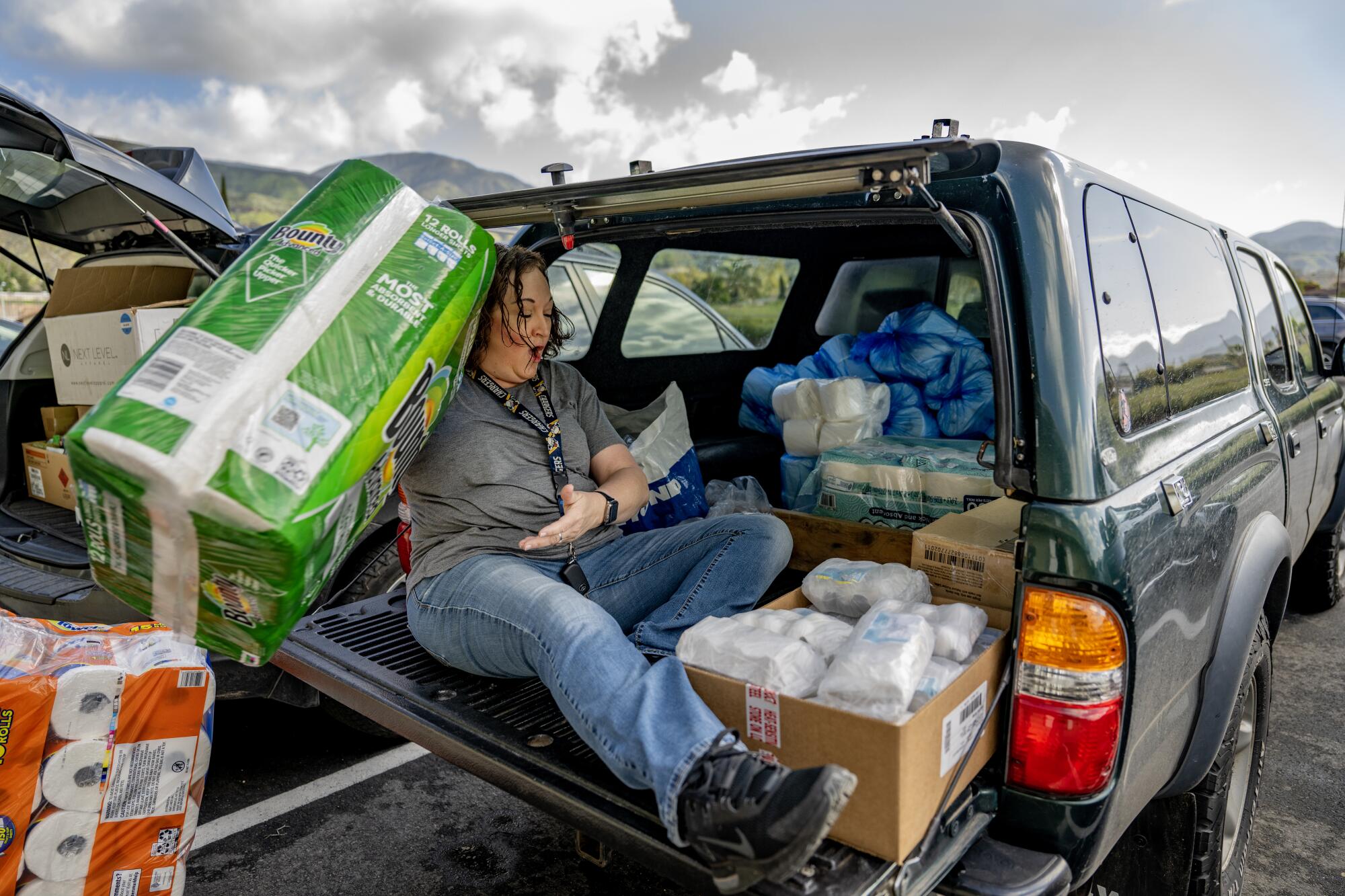 A woman sits in the back of an SUV with boxes of toilet paper and packages of paper towels.