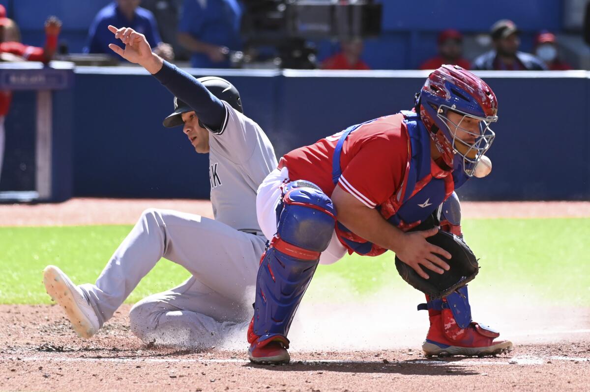 New York Yankees' Isiah Kiner-Falefa, left, slides safely into home ahead of a tag by Toronto Blue Jays catcher Alejandro Kirk, right, after a three-RBI double by Aaron Hicks in the fourth inning of a baseball game in Toronto, Saturday, June 18, 2022. (Jon Blacker/The Canadian Press via AP)
