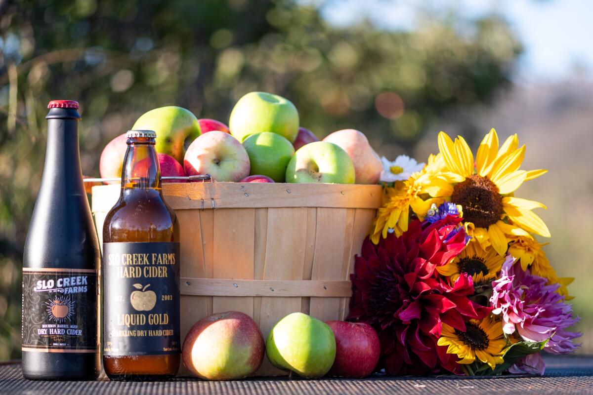 A basket of apples next to two cider bottles and cut flowers