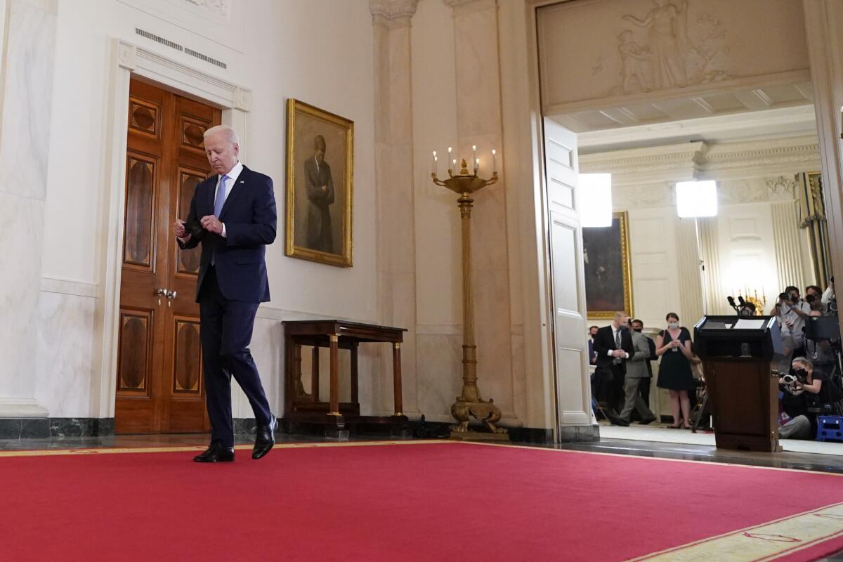 President Biden walks on a red carpet away from a lectern with reporters in front of it