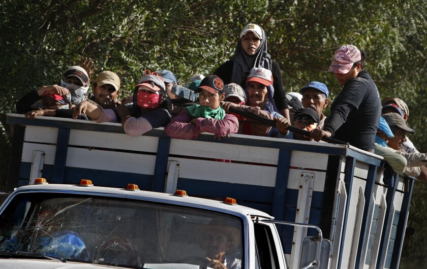 Farmworkers stand in an open-bed truck.