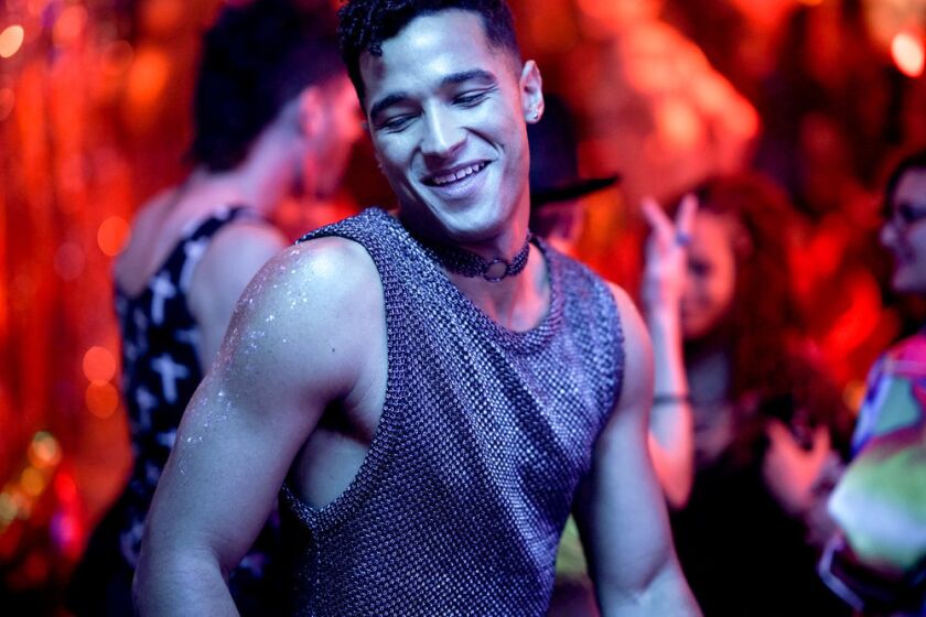 A man in a glittering sleeveless top with glitter on his arms dancing at a club