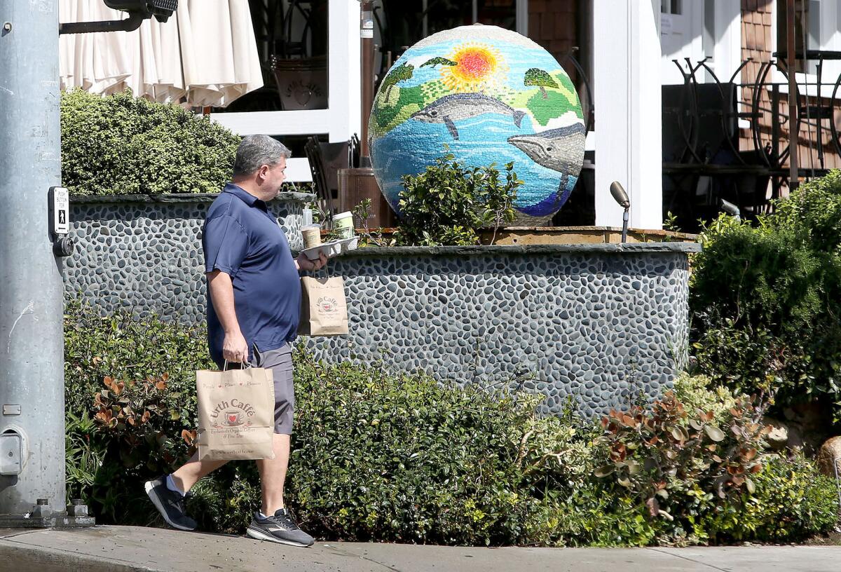 A patron of Urth Caffe in Laguna Beach carries a takeout order as local restaurants and other essential businesses comply with orders to prevent gatherings during the coronavirus pandemic.