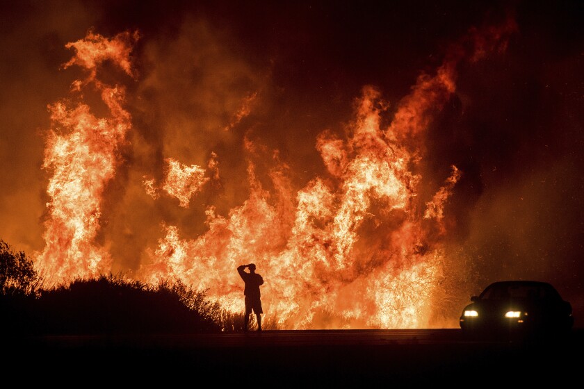 FILE - A motorists on Highway 101 watches flames from the Thomas fire leap above the roadway north of Ventura, Calif., on Dec. 6, 2017. Southern California Edison has reached an agreement with state regulators on Thursday, Dec. 16 2021, for more than half a billion dollars in penalties related to five wildfires, including the Thomas fire. (AP Photo/Noah Berger, File)