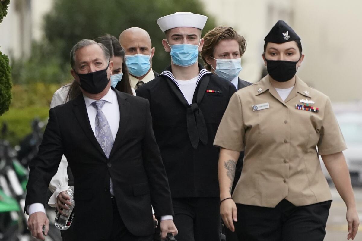 People wearing suits and Navy uniforms walk with masks on