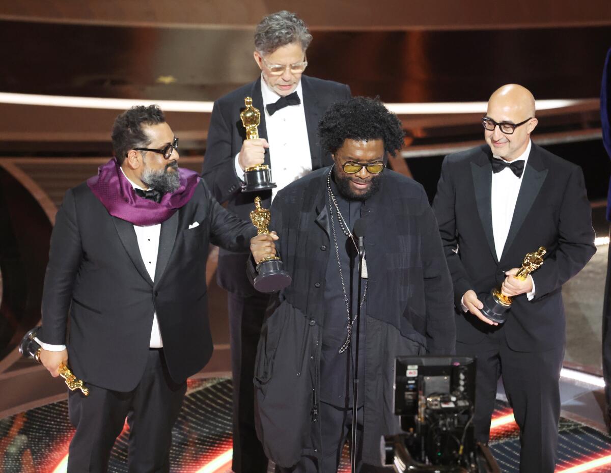 Four men in tuxedos stand onstage holding Oscar statuettes