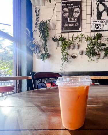 A plastic lidded cup of orange liquid sits on a wood table, sunlight streaming in from the nearby window