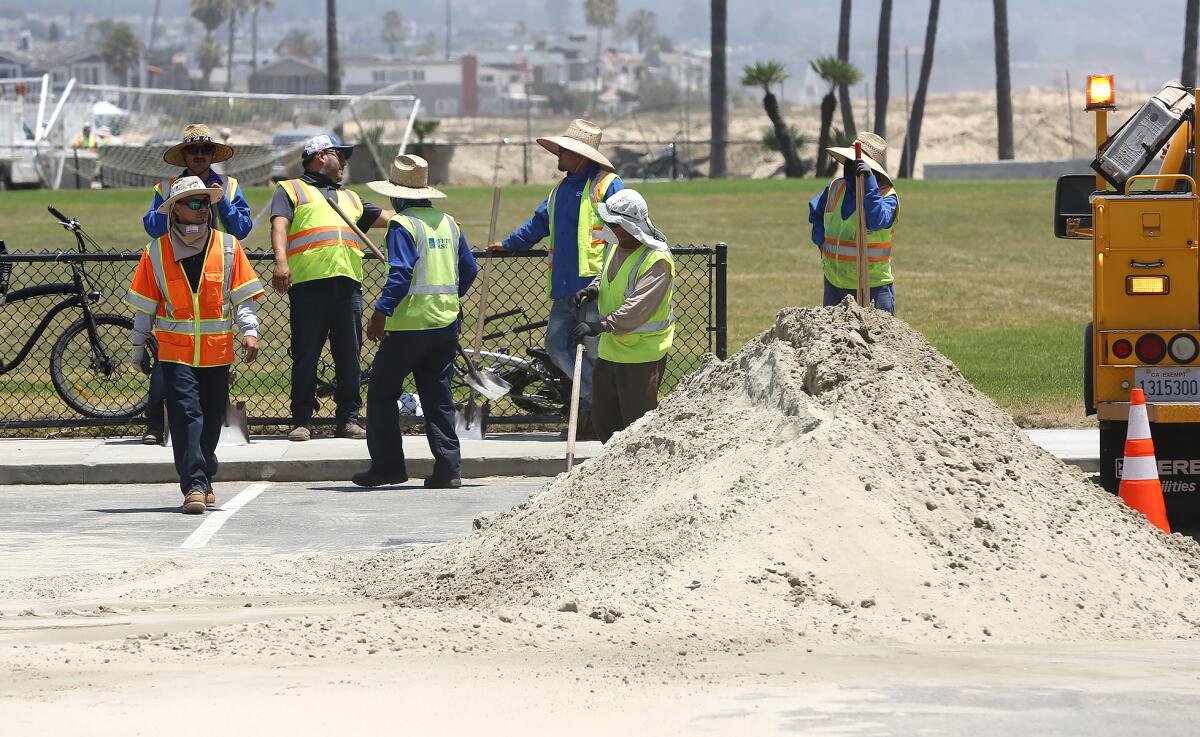 Workers clear sand and debris as a result of the flooding that occurred on Friday in Newport Beach.