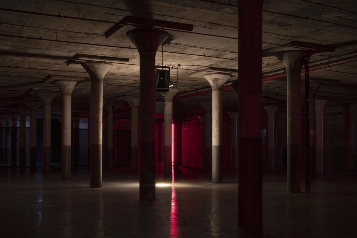 A dark empty space with several floor-to-ceiling columns and a pink line of light in the middle