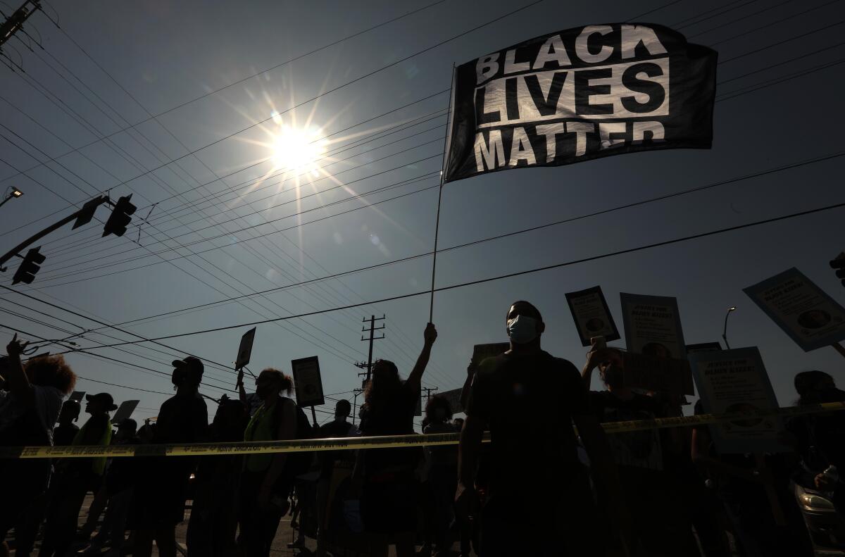 Silhouettes of people at a demonstration. One holds a Black Lives Matter flag.