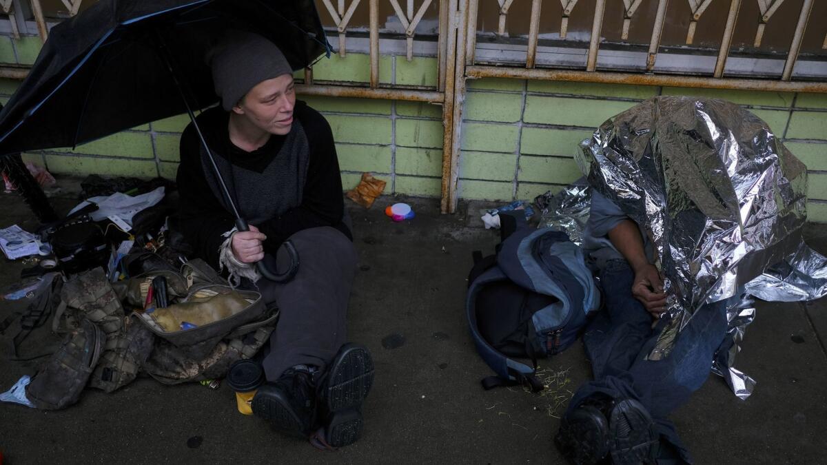 Cristal, 31, left, sits on a skid row sidewalk in downtown L.A. on a recent cold, rainy day.