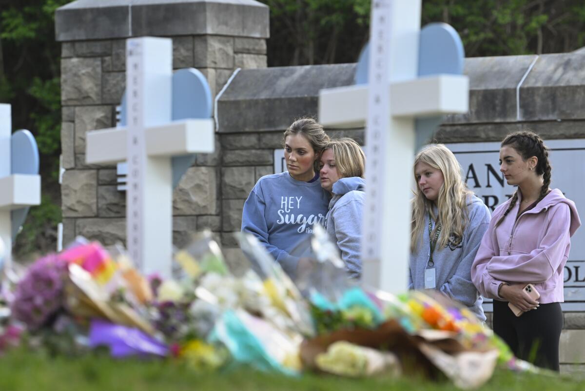 Four girls mournfully look at a memorial of three crosses 