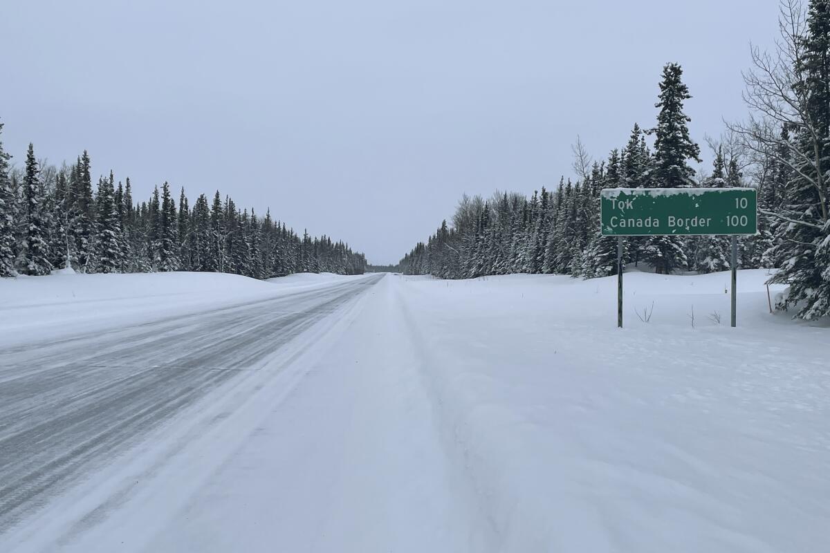 A snowy road with a sign reading 10 miles to Tok, Alaska, and 100 miles to the Canada border. 