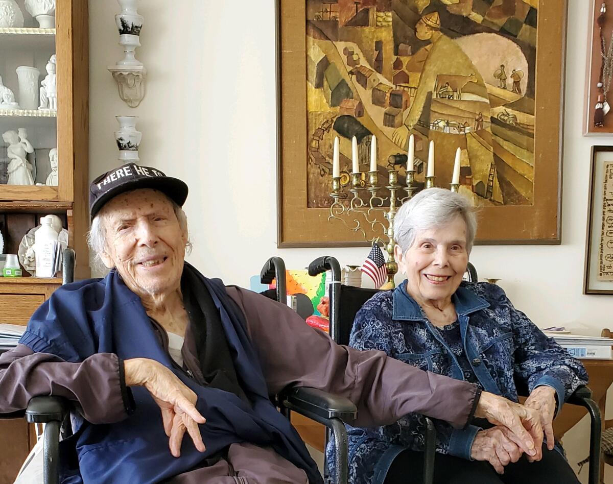 Norman and Sivia Mann smile as they sit side-by-side in wheelchairs at home
