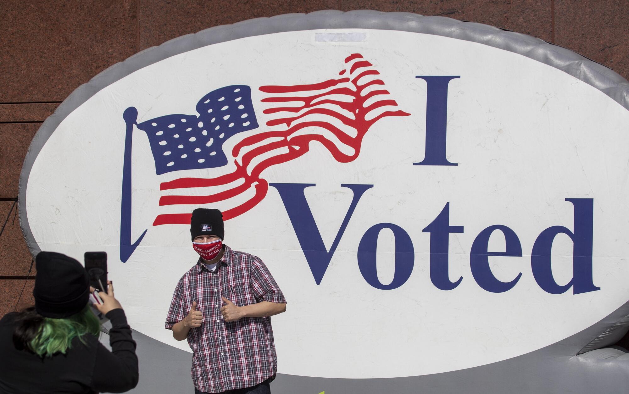 A man poses for a photo in front of a giant I Voted image.