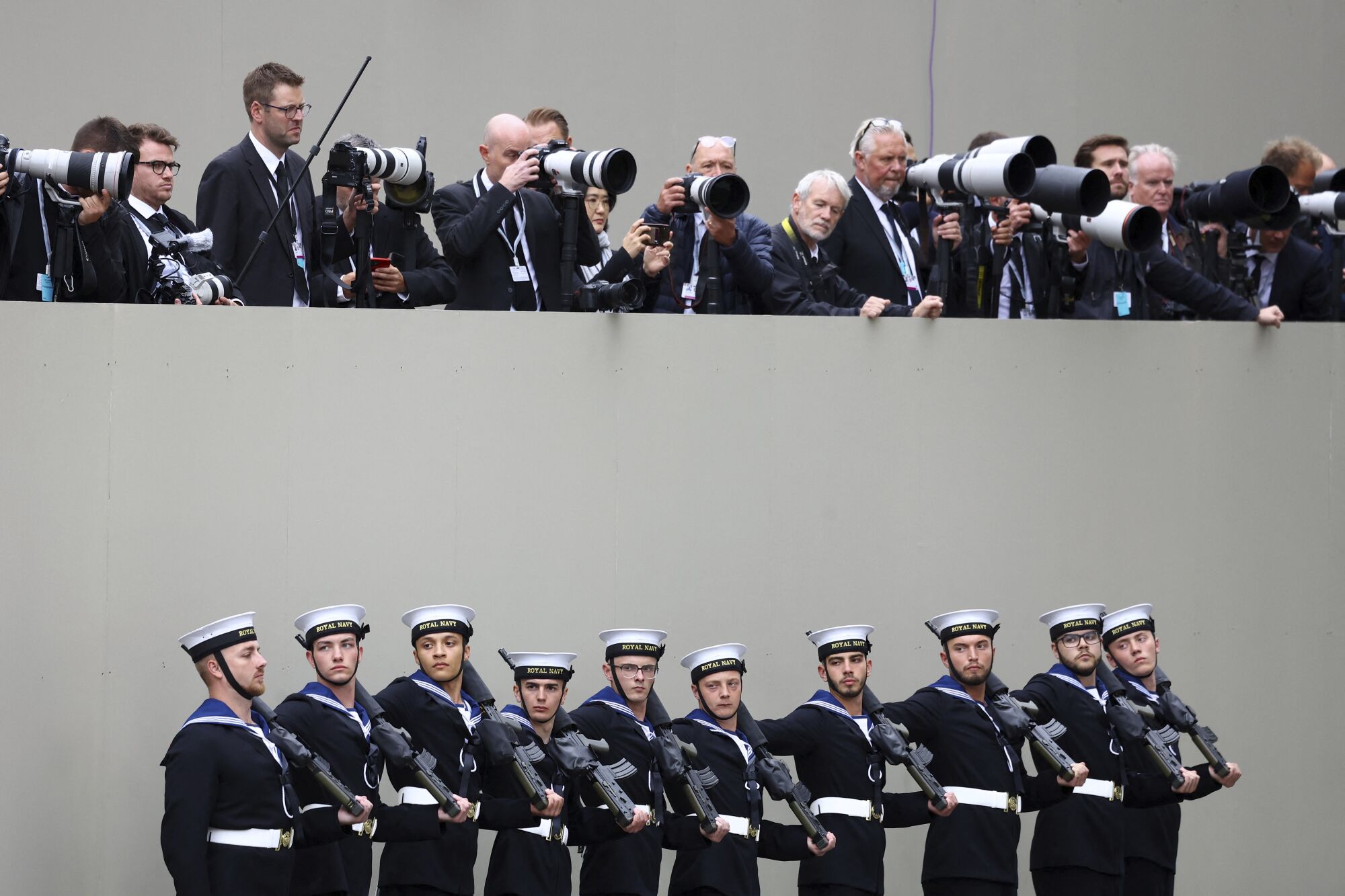 Des membres de la Royal Navy se tiennent sous la rangée de photographes. 