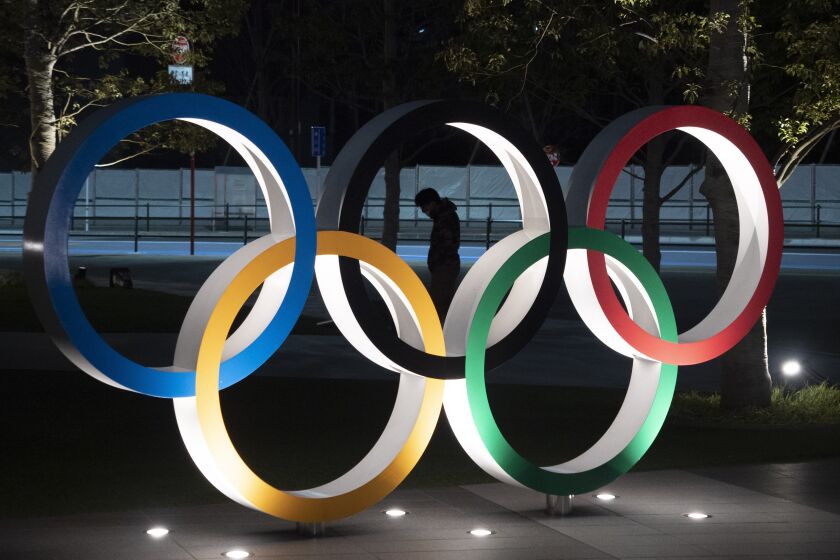 FILE - In this March 24, 2020, a man is seen through the Olympic rings.