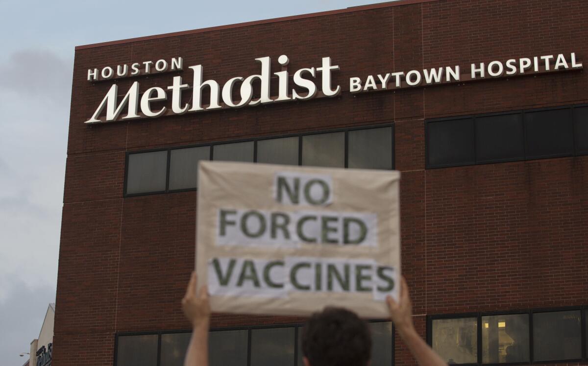 A person holds a sign that says "No forced vaccines" in front of a hospital