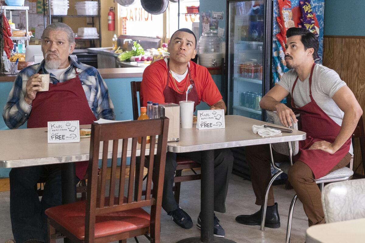 Three men sit at a table in a diner, looking up.