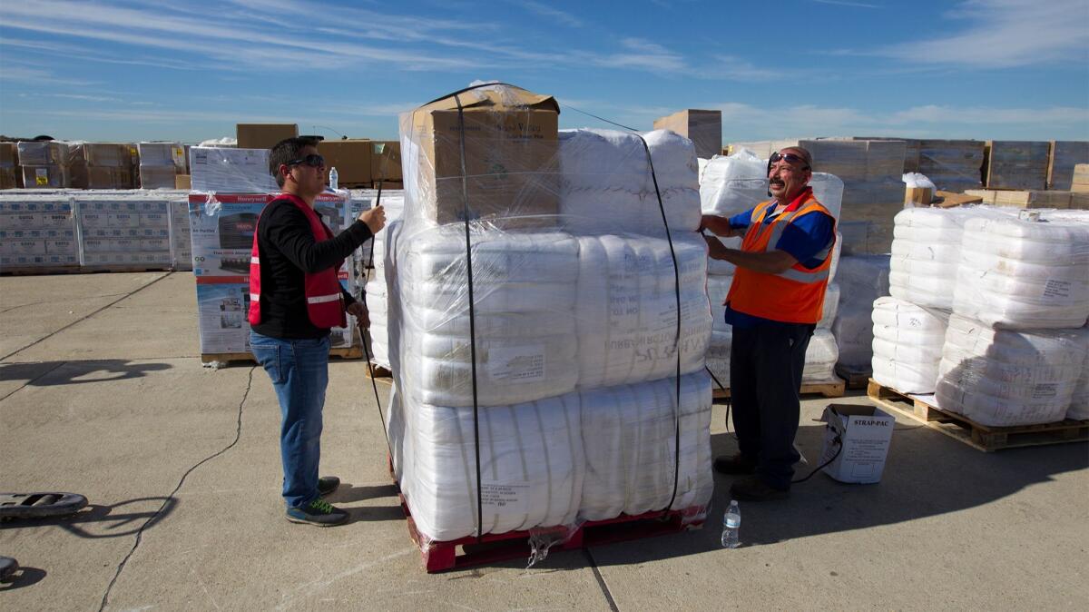 Salvador Meza, left, and Ariel Zatarain with Estes Express, a trucking company, repackage supplies destined for evacuation centers in wildfire zones throughout the state. The supplies are being stored at the Joint Forces Training Base at Los Alamitos.