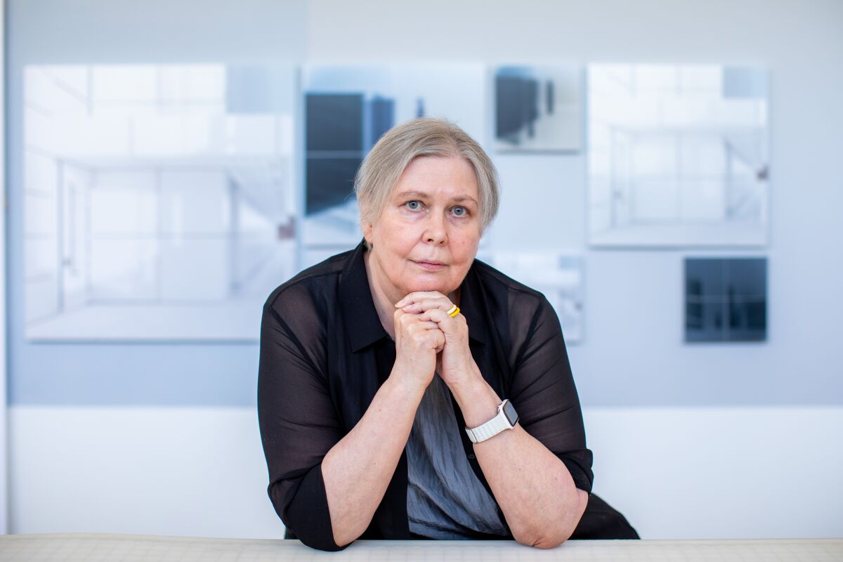 Uta Barth leans her chin on her hands as she sits before a series of images suspended on the wall behind her