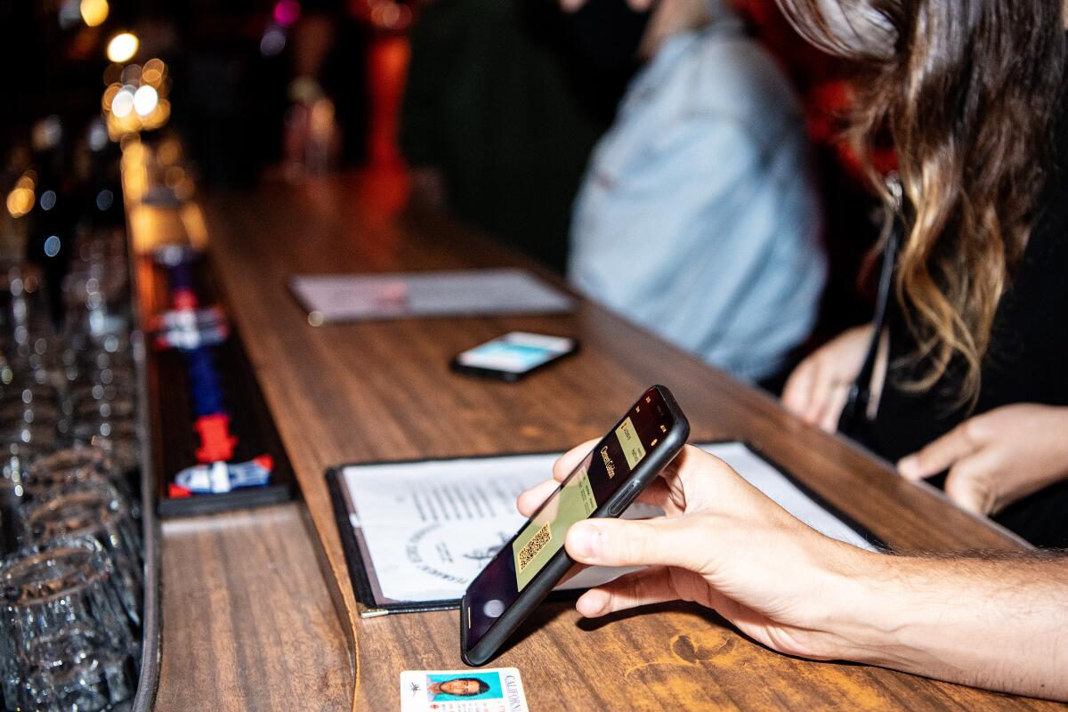 A bar patron shows a phone and ID to a bartender