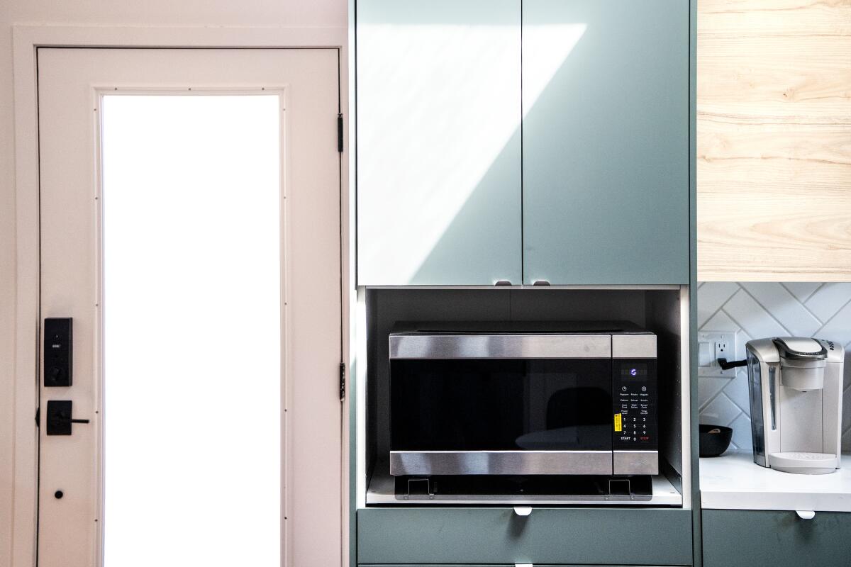 A silver microwave below a green cabinet sits next to a door.