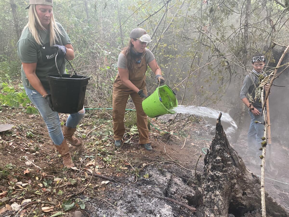 A woman tosses a bucket of water on a smoldering hot spot in the woods