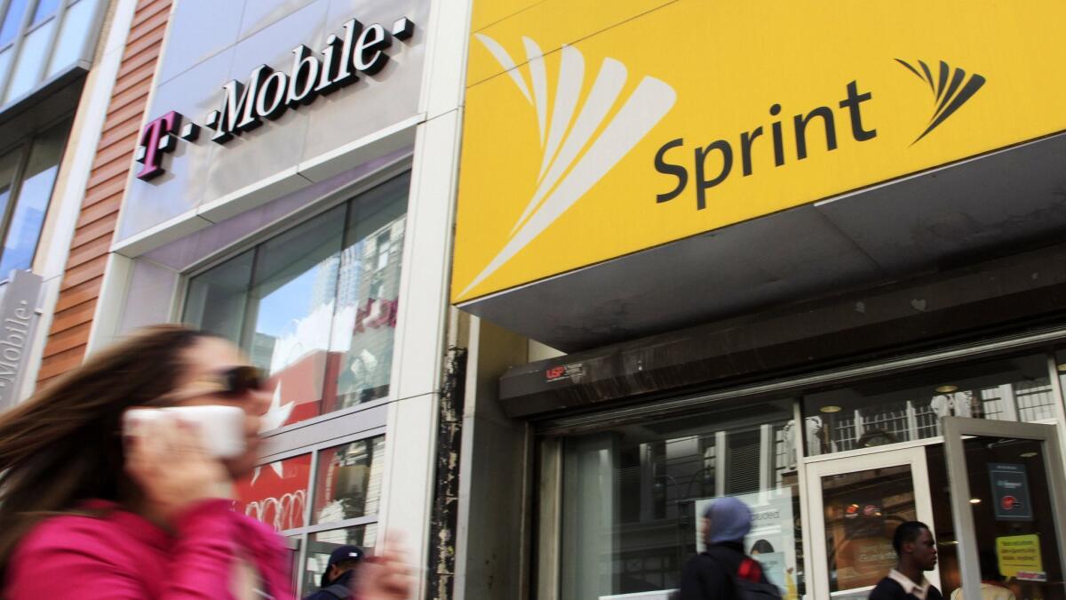 A woman using a cell phone walks past T-Mobile and Sprint stores in New York in 2010.