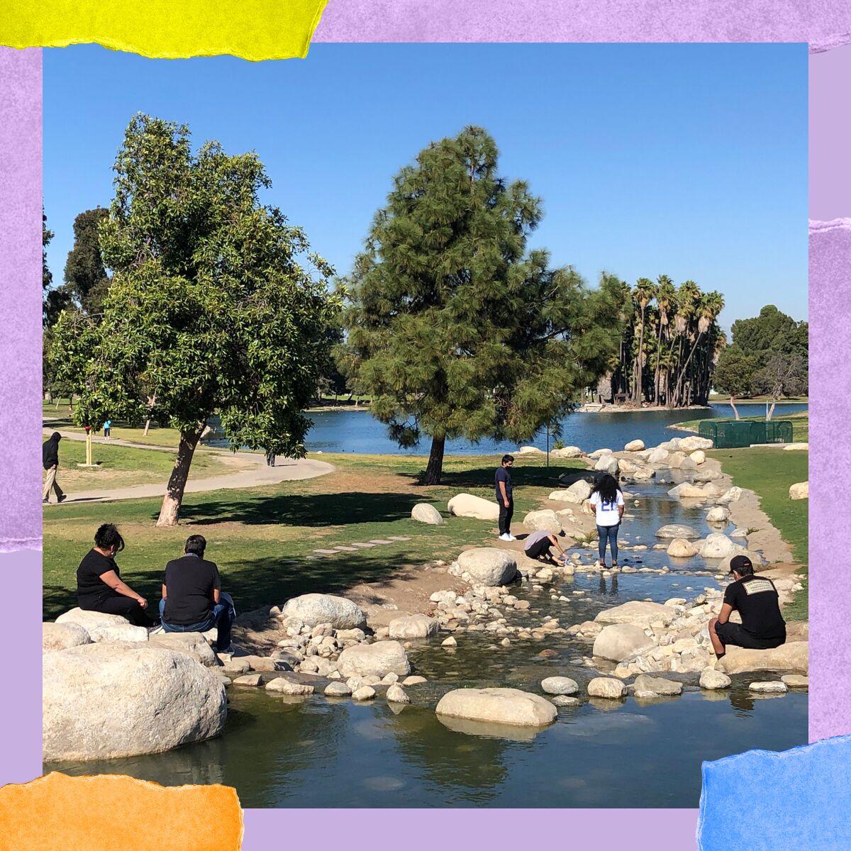 Park patrons sit on rocks and boulders in a set of shallows that connect the two lakes in Magic Johnson Park