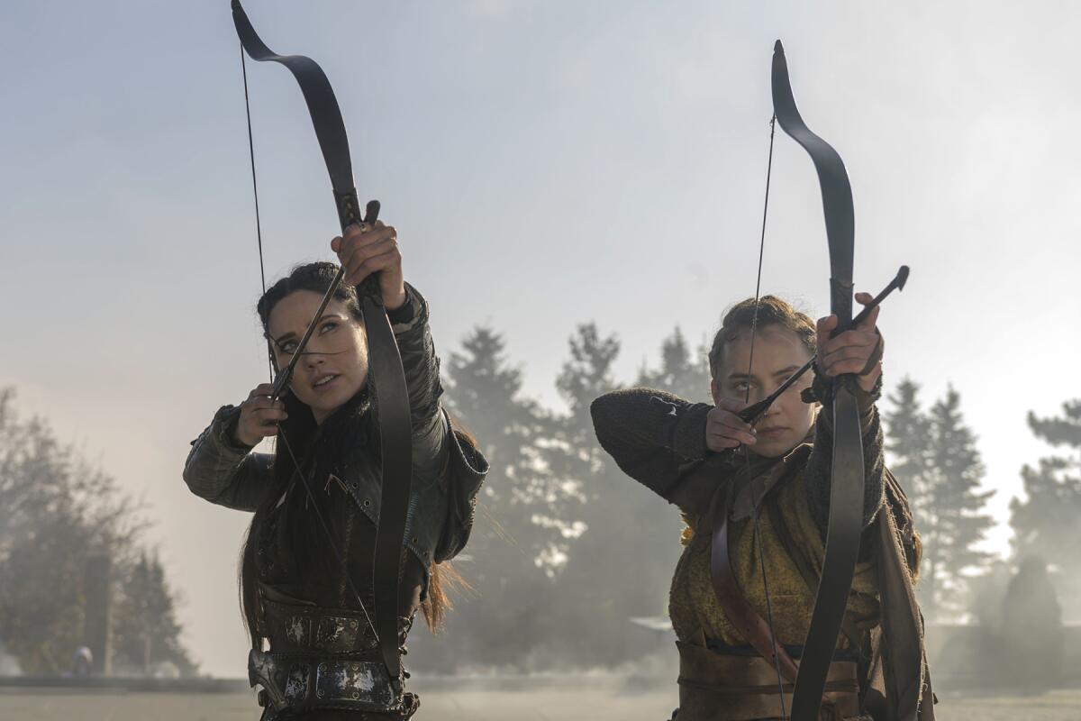 Two young archers notch arrows and draw their bows.
