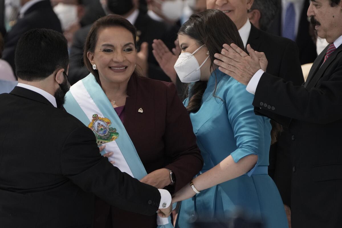 La presidenta Xiomara Castro sonríe mientras recibe la banda presidencial, mientras su esposo