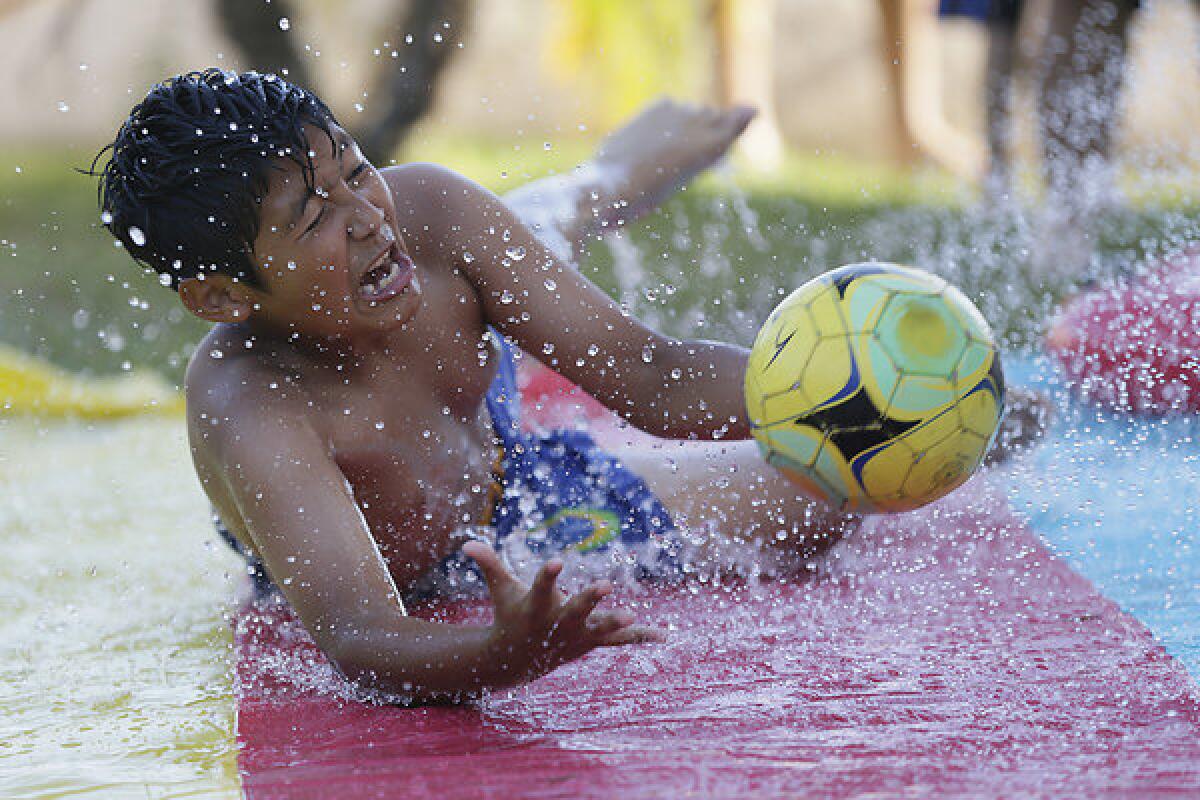 Jose Baltazar, 11, joins friends and relatives in a respite from high temperatures as they frolic on a lawn water slide in Azusa.