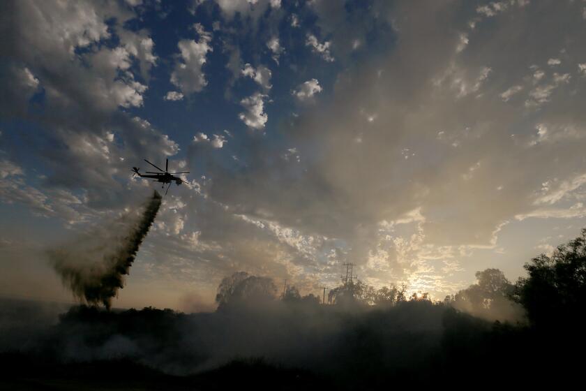 A firefighting helicopter makes a water drop on a wildfire burning in the hills around Idaho Street in La Habra.