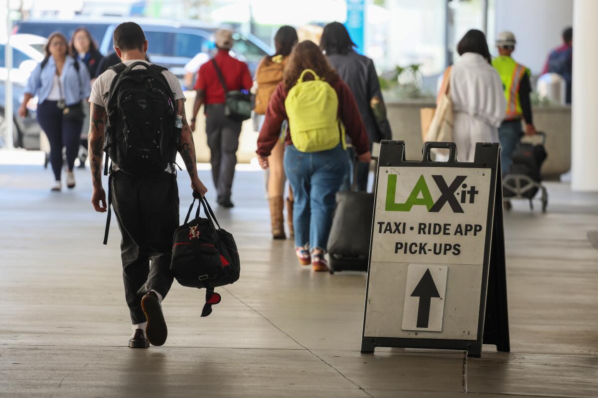 Travelers with suitcases and backpacks walk past a sign pointing to the LAX-it lot.
